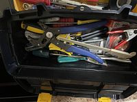 Open black Stanley toolbox with pliers, wire cutters, utility knife, screwdrivers, and other hand tools inside