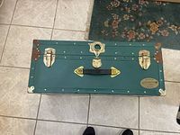 Top view of green steamer trunk showing latch, locks, handle, brass hardware, and minor rust on corners