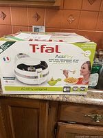 Box of T-fal ActiFry air fryer on kitchen counter, showing front and top of packaging with images and branding.