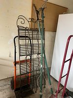 Photo showing two moving dollies, two green tree trimmers with cutting blades and ropes, and a black metal trellis with scroll design.