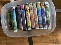 Clear photo showing all 12 VHS tapes arranged standing side by side inside a plastic bin