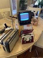 Curtis portable TV displaying static on screen, Nordmende radio, and red vintage radio with flip-up lid on wooden table