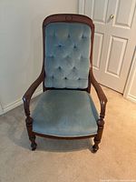 Front view of antique wooden armchair with blue tufted backrest and cushioned seat.