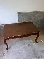 Photo showing the antique wooden coffee table from above, highlighting the carved edge top and graceful cabriole legs.