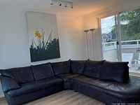 Photo of aubergine leather sectional sofa arranged in L shape in living room with visible cushions and floor lamp nearby