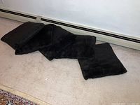 Five dark brown faux fur pillows laid out on carpeted floor in a row, showing size and texture.
