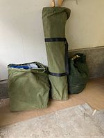 Three closed green canvas storage sacks standing against a wall