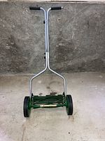 Front view showing the overall structure of the hand lawn mower, including the metal frame, wheels, handle, and blade housing.