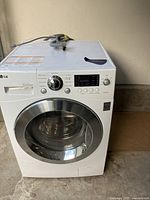 White front-loading LG Inverter Direct Drive washer and dryer combo with hoses on top, placed on concrete floor