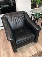 Front angle view of one black leather arm chair showing its design, leather texture and padding.