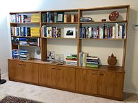 Front view of the New Zealand Kauri wood custom bookcase cabinet unit filled with books and decorative items on shelves, closed wooden cabinets below.