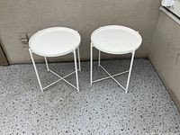 Two white patio side tables with removable tray tops shown outdoors on a speckled concrete floor.