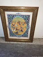 Photo of the framed Persian miniature art print resting against a wall, showing the full front view of the piece including the frame and detailed central painting.