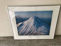 Framed photo of snow-capped Mt Taranaki in Egmont National Park, New Zealand, placed against a wall.