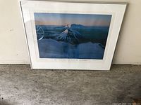 Framed photo of Mt Ruapehu and Mt Noughton mountains in New Zealand leaning against a white wall on a gray floor.