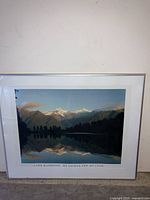 Framed photographic print showing Lake Matheson with Mt Tasman and Mt Cook mountains under blue sky and reflected in lake.