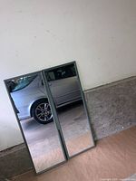 Photo of two rectangular mirrors leaning against a wall, showing their reflective surfaces and metal frames.