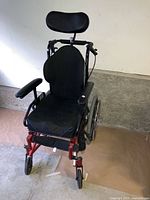 Front angle photo of a lightweight manual wheelchair with padded seat, headrest, armrests, and wheels on concrete floor