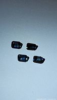 Four emerald cut blue sapphires shown on a white background under lighting to show color and cut clearly