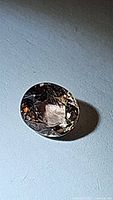 Close-up photo of oval cut pinkish-orange champagne colored sapphire on a light background.