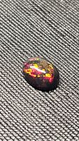 Close-up photo of 1.21ct natural oval cabochon Ethiopian black opal showing vivid flashes of red, yellow, and green colors on a black base.