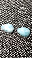 Pair of natural pear-shaped larimar cabochon gemstones on a textured black background showing their light blue and white marbled coloring and polished surface.