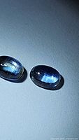 Pair of natural oval cabochon blue sapphires with visible internal inclusions and deep blue color under direct light.