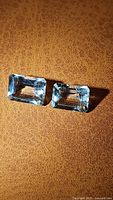 Pair of rectangular cut natural aquamarine gemstones on brown textured surface.
