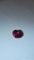 Close-up image showing oval cut ruby gemstone with deep red color and visible inclusions.