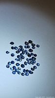 Image showing numerous small, loose natural blue sapphire stones in diamond cut on white background.