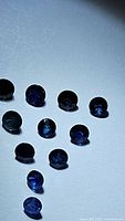 Oval round deep blue faceted sapphires laid out on a white surface, showing different angles and light reflections