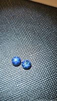 Two round blue star sapphires on textured black surface, showing six-rayed star effect on polished cabochon cut stones.