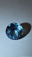 Faceted round cut natural sky blue topaz gemstone, around 10mm diameter, shown from multiple angles under lighting to display clarity and color.