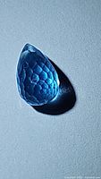 Close-up image of a single teardrop-shaped blue topaz gemstone with detailed faceting and drilled top.