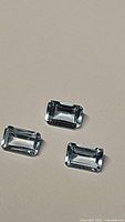 Top view of three natural blue topaz gemstones with emerald cut, showing clear light blue color and clean facets.
