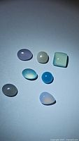 Top down view of ten polished natural chalcedony gemstones in various blue, white, and purple shades with different shapes including oval, round, square, and pear