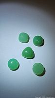 Top view of the five green chrysoprase gemstones in different shapes and sizes arranged on white surface