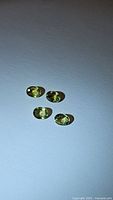 Four oval cut natural sapphires in chartreuse mint green on white background with visible facets and high clarity.