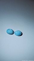 Pair of oval natural Larimar cabochon gemstones on a plain background showing their light blue color and white marbling.