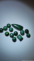 Various polished malachite stones displayed on a plain surface showing natural banding and green coloration under focused light.