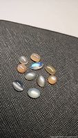 Cluster of 11 assorted natural moonstone cabochons showing a variety of colors and translucency, including a blue flash rainbow stone.