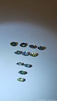 Ten small faceted sapphires arranged on a light surface showing various colors including blue, yellow, and greenish tones.