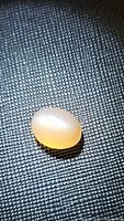 Oval peach moonstone cabochon resting on textured surface showing translucent peach tone and catseye flash effect