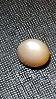 Oval cabochon peach moonstone gemstone placed on textured black background. Shows glossy, smooth polished surface with peach hue and reflective flash.