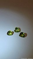 Three natural pear-shaped apple green peridot gemstones placed on a white background under direct lighting, showing their faceted cuts and vibrant green color.
