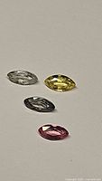 Four natural marquis cut sapphires in clear, yellow, bluish-gray, and pink colors arranged on a plain white background.