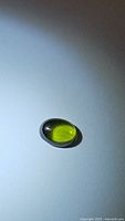 Oval cabochon natural chrome diopside gemstone under light showing vivid translucent green color and internal reflections.