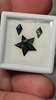 Top view of five kite cut green sapphires displayed on white surface inside a small display box held in hand.
