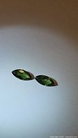 Pair of two marquis cut green sapphires laid flat on white background, showing their shape, color, and clarity.