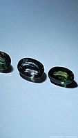 Three oval-cut sapphire gemstones arranged on a light background showing green, champagne, and purple colors.
